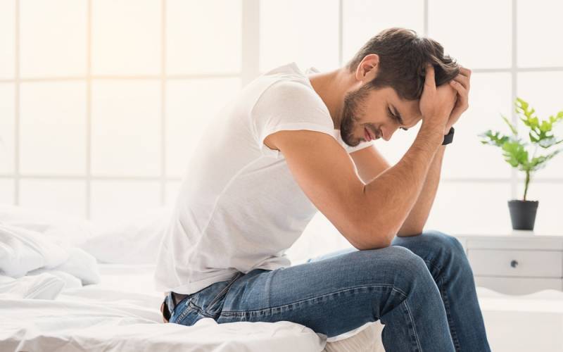 Un hombre sentado en la cama se muestra cansado y con dolor de cabeza